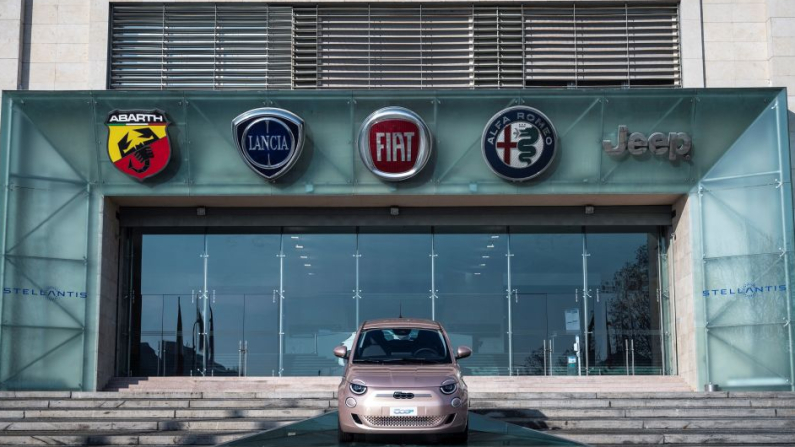 A picture taken on January 19, 2021 shows the logos of automobile companies (LtoR) Abarth, Lancia, Fiat, Alfa Romeo and Jeep and a newly-added board with the name of Stellantis, the company forged in mega-merger of Fiat and Peugeot, at the entrance of the Fiat Mirafiori car plant in Turin, northern Italy. The Prima 500 electric car is seen in the foreground. Stellantis, a new company from the merger of Fiat Chrysler and PSA creates the 4th largest automobile group in the world. (Photo by Marco Bertorello / AFP) (Photo by MARCO BERTORELLO/AFP via Getty Images)